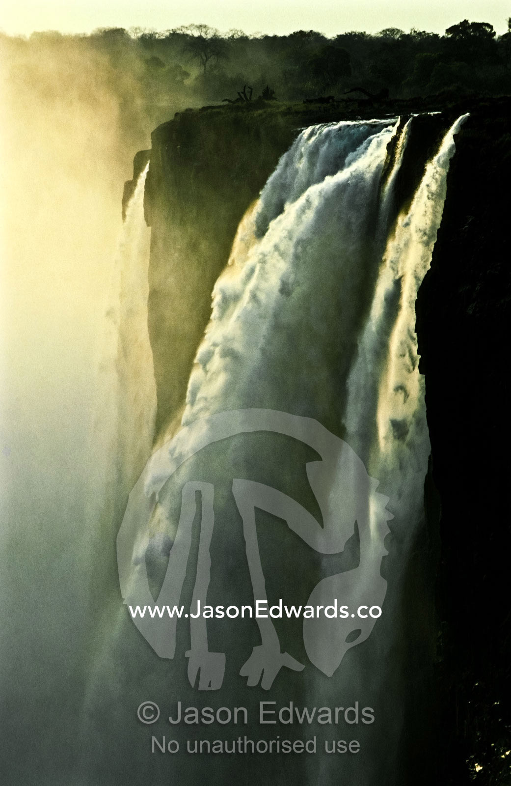 Sunset illuminates pillars of water cascading over Victoria Falls. Victoria Falls National Park, Zimbabwe.