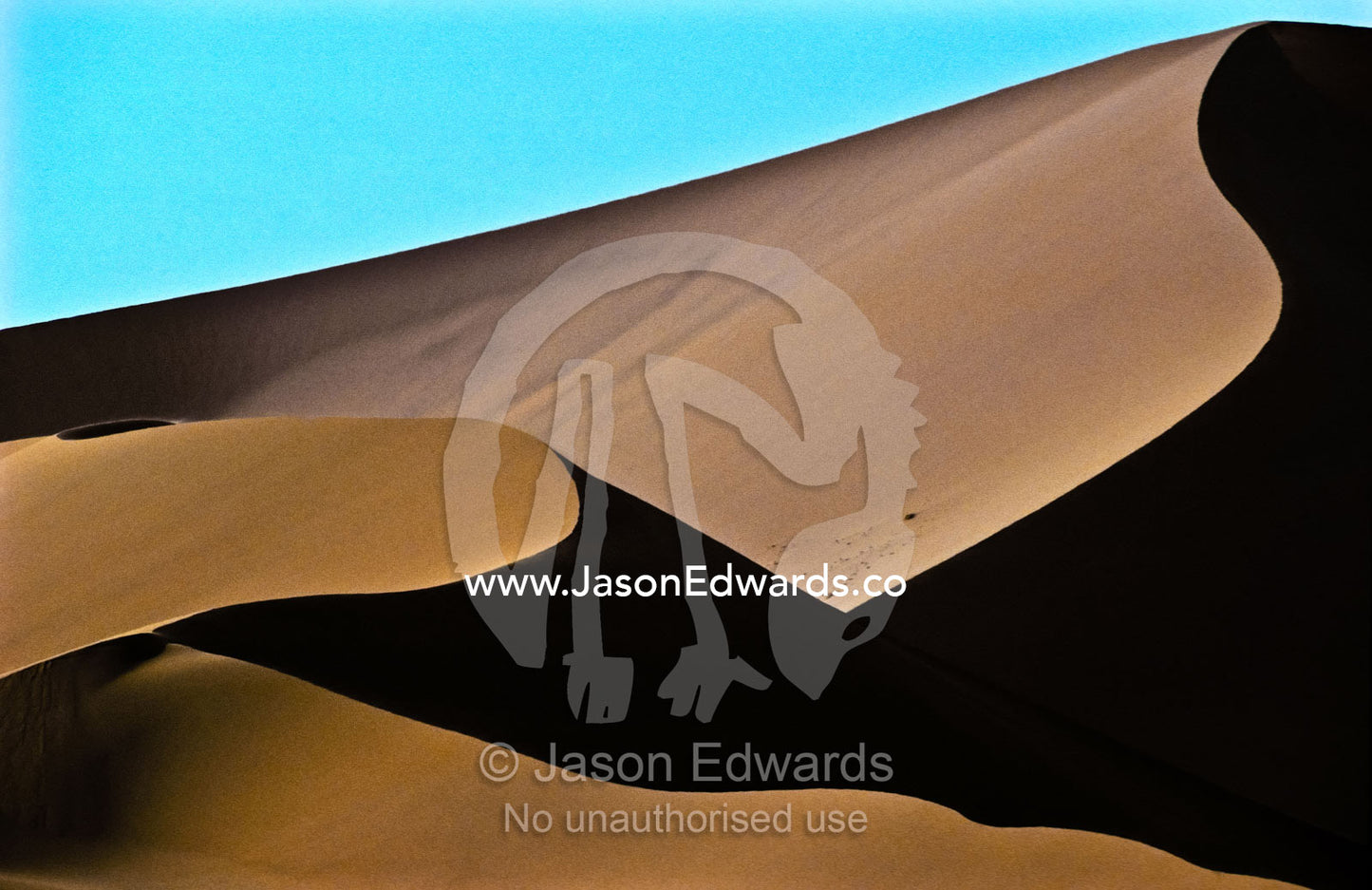 The elegant crest of a vast sand dune in shadow against a blue sky. near Sossusvlei, Great Southern Dune Field, Namib-Naukluft National Park, Namibia.
