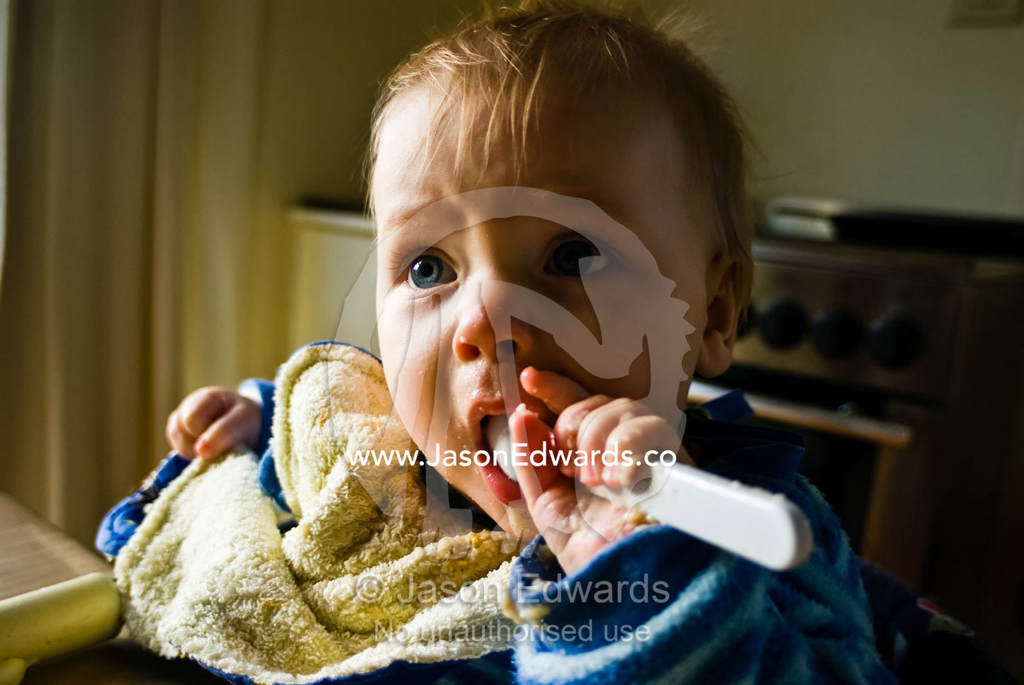 A baby learns to feed himself solid food using a spoon. Castlemaine, Victoria, Australia.