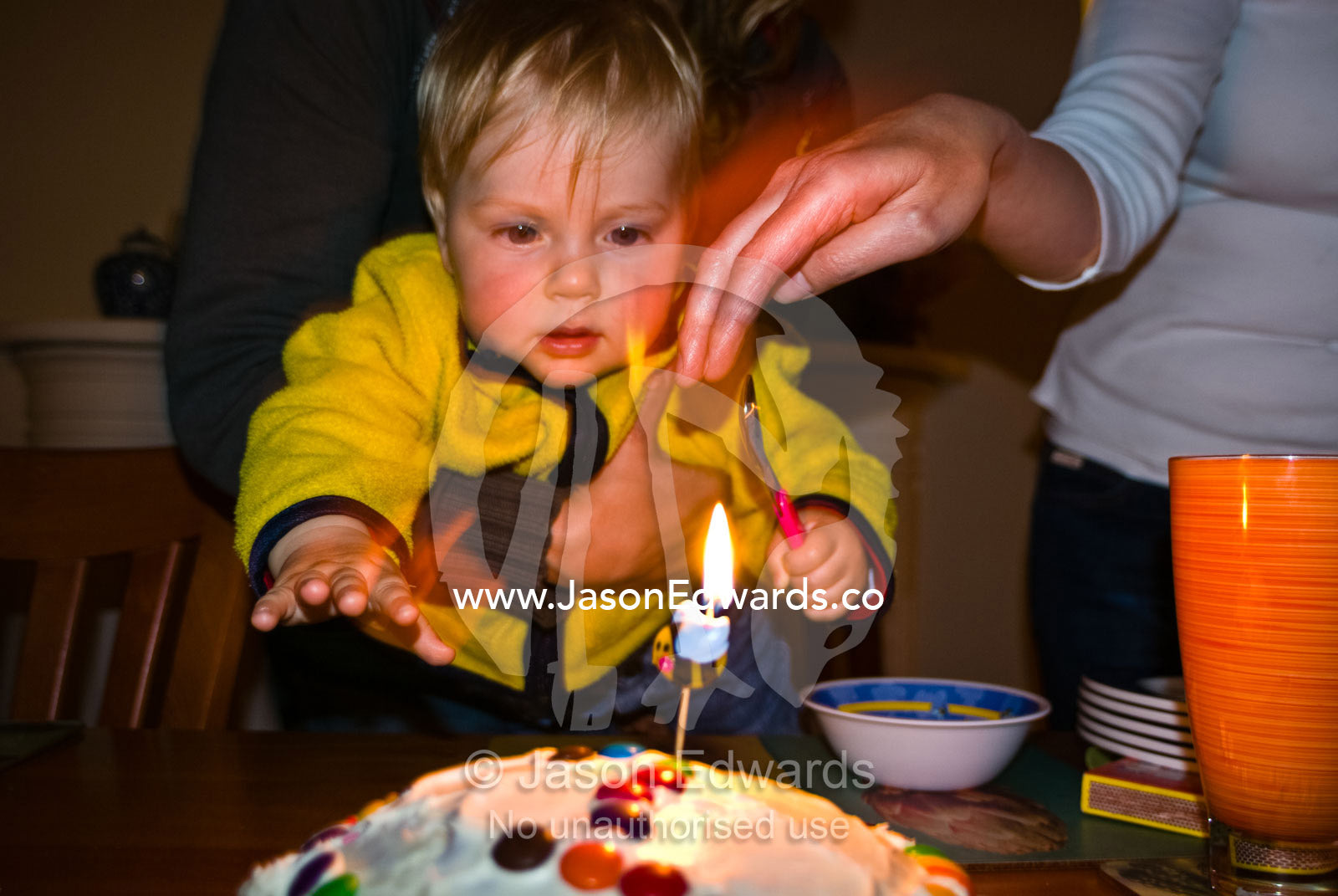 A parent stops a toddler from burning his fingers on a birthday cake. Mount Waverley, Victoria, Australia.