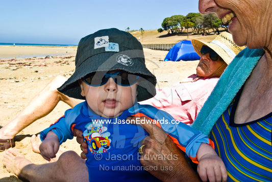 A baby enjoys a summer's day on the beach with his grandparents. Cosy Corner, Torquay, Victoria, Australia.