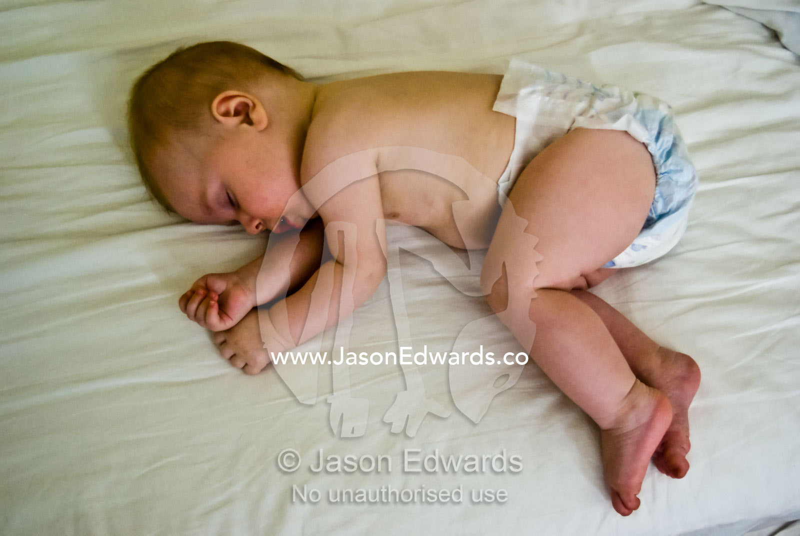 An exhausted baby having a morning sleep on his parents bed in summer. North Carlton, Victoria, Australia.