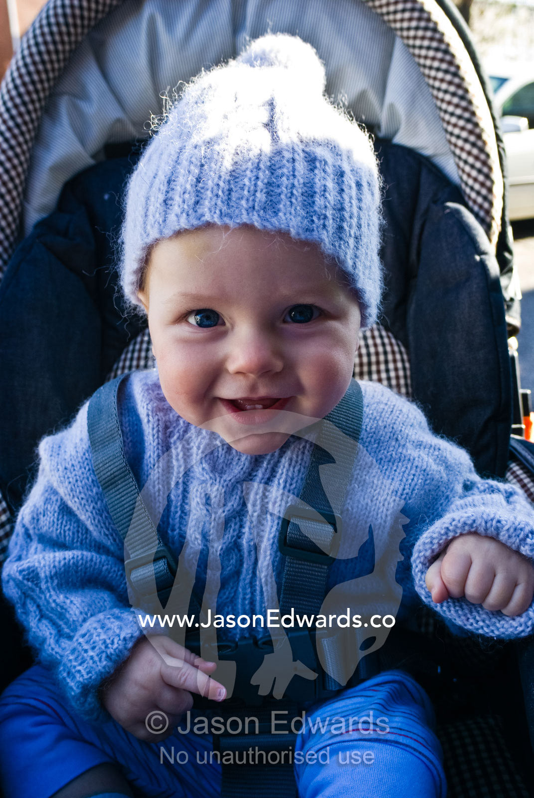 A beaming baby bundled up in woolens prepares for a walk in a stroller Carlton North, Victoria, Australia.