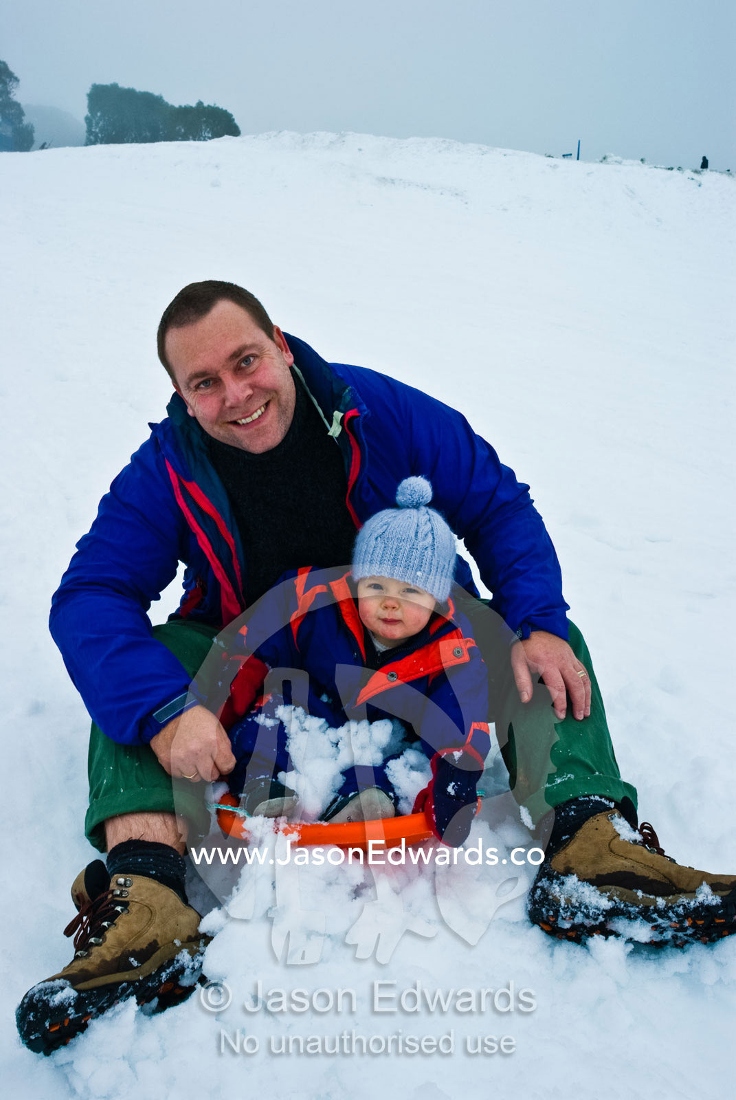 A father and son enjoy riding a toboggan in an alpine ski resort. Falls Creek, Alpine National Park, Victoria, Australia.