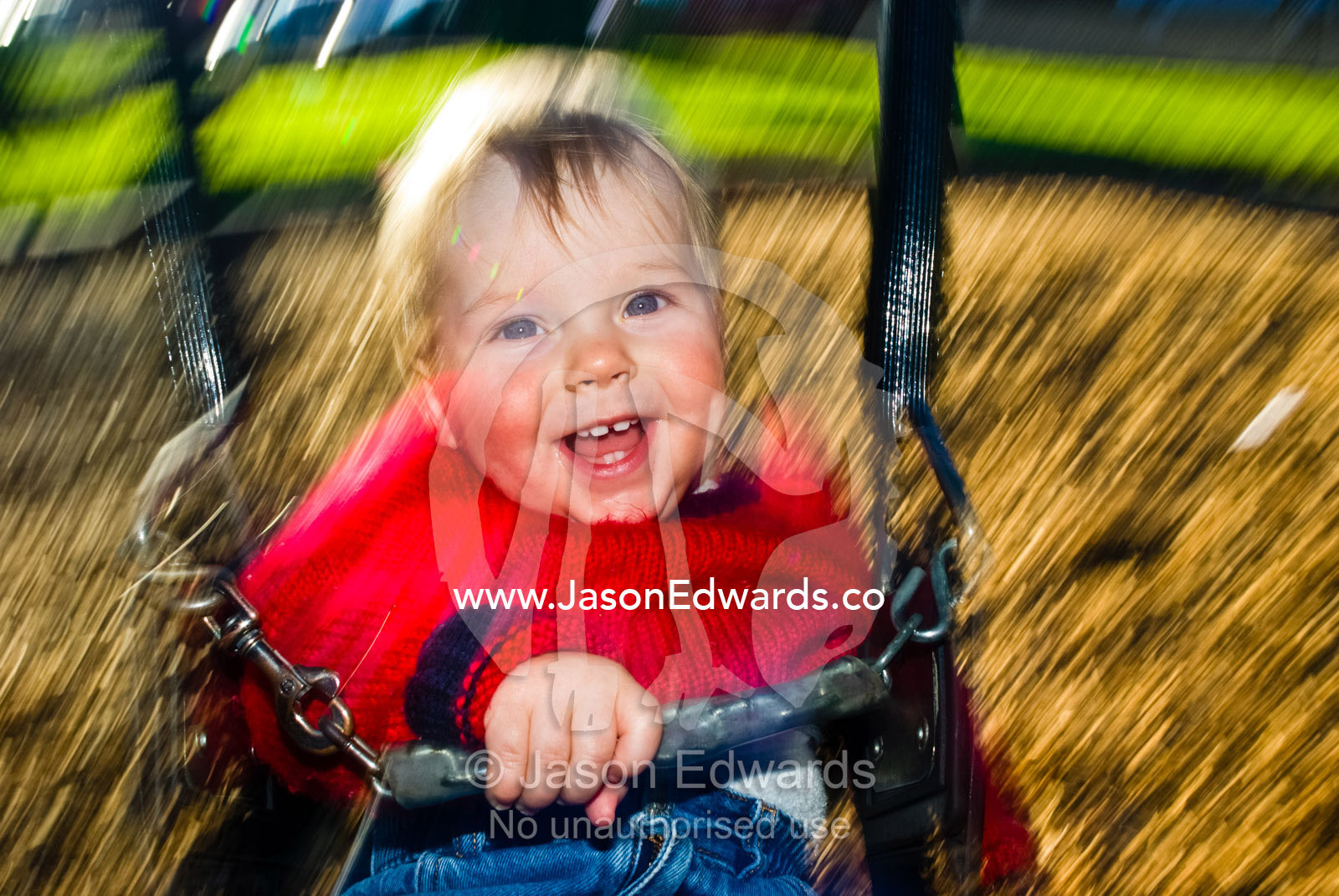 A baby's ecstatic grin as he swirls around on a playground swing. Curtain Square, North Carlton, Victoria, Australia.