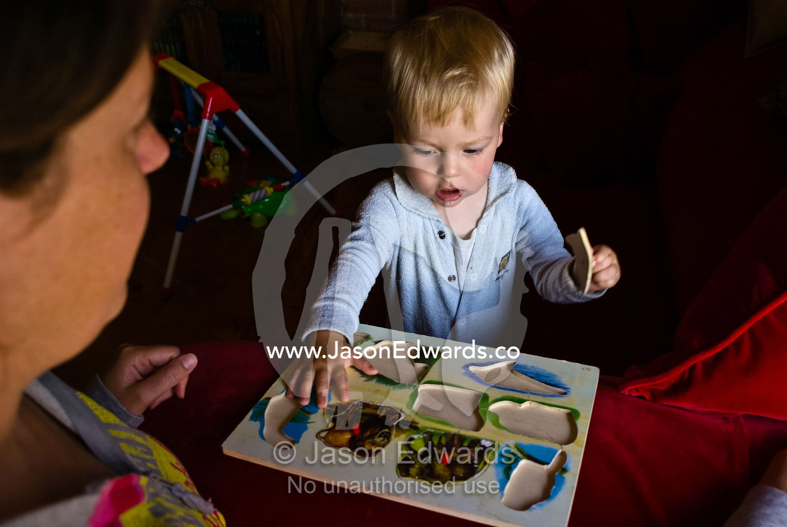 A toddler works on an animal puzzle whilst his mother proudly watches. Carlton North, Victoria, Australia.