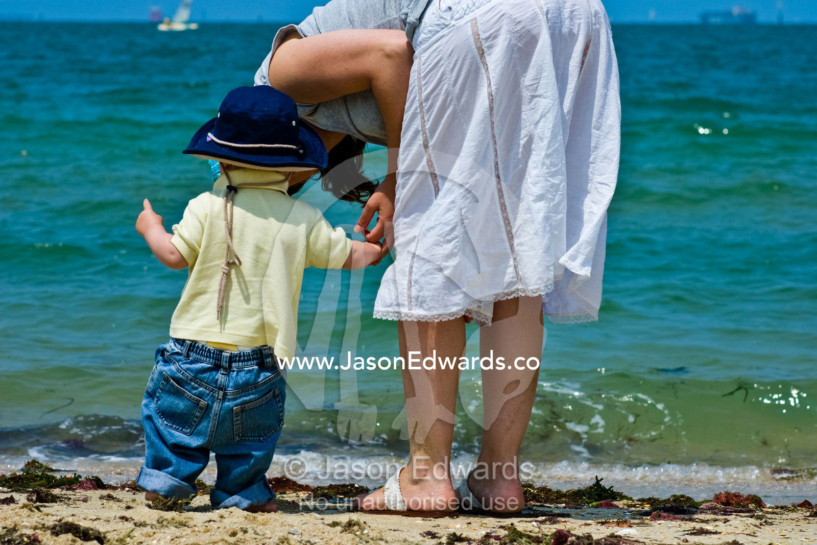 A mother gently kisses her son whilst exploring the beach and waves. Port Melbourne, Victoria, Australia.