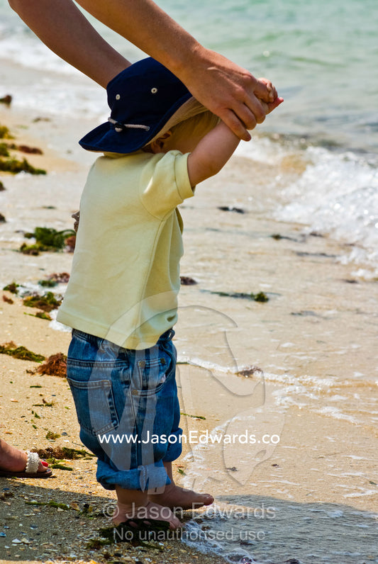 A mother holds her sons hand whilst exploring the beach and waves. Port Melbourne, Victoria, Australia.