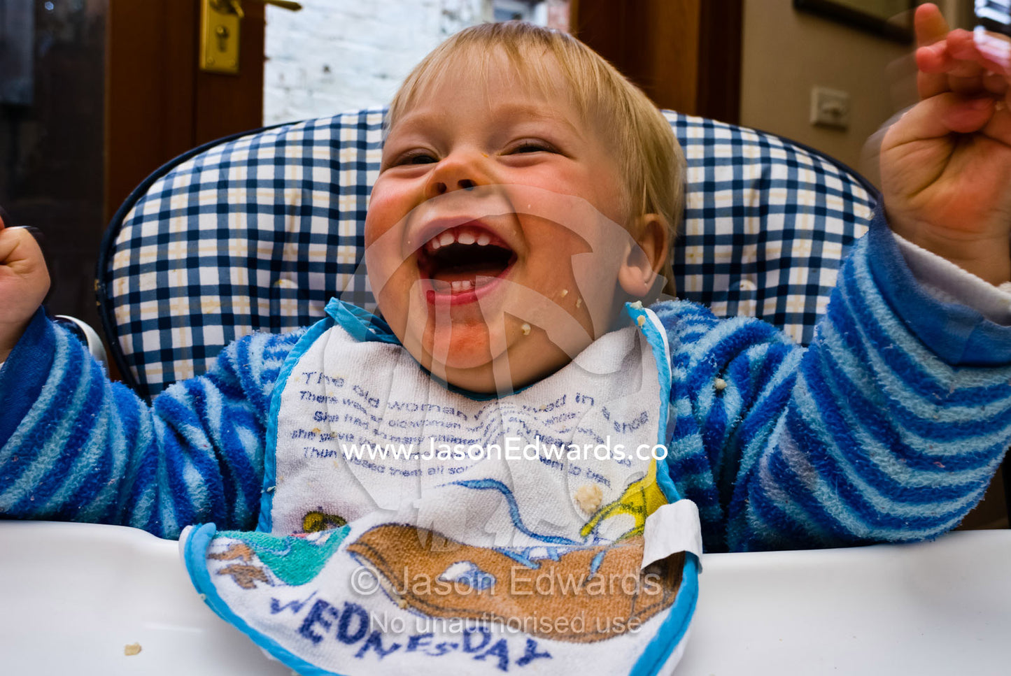 A young boy with food on his face laughs hysterically at breakfast. Carlton North, Victoria, Australia.