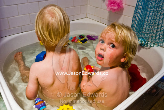 Two fair-skinned, fair-haired friends take a bath with their toys. Carlton North, Victoria, Australia.