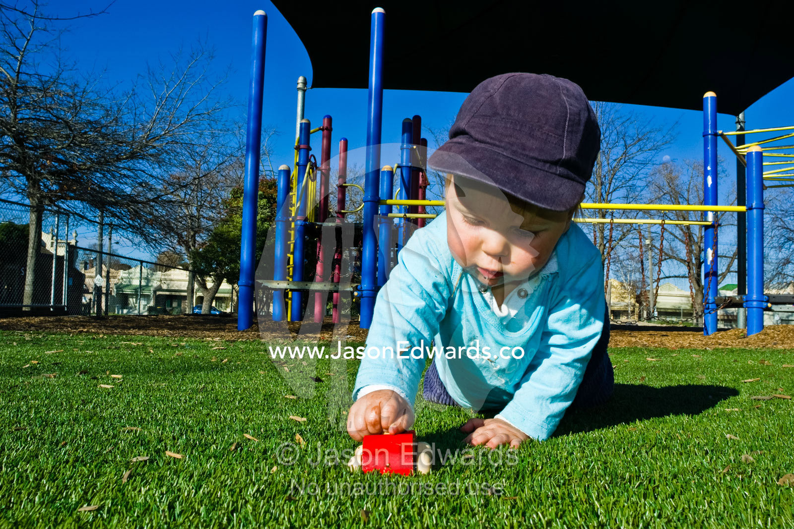 A young boy focuses on playing with his wooden car in a playground. Carlton North, Victoria, Australia.
