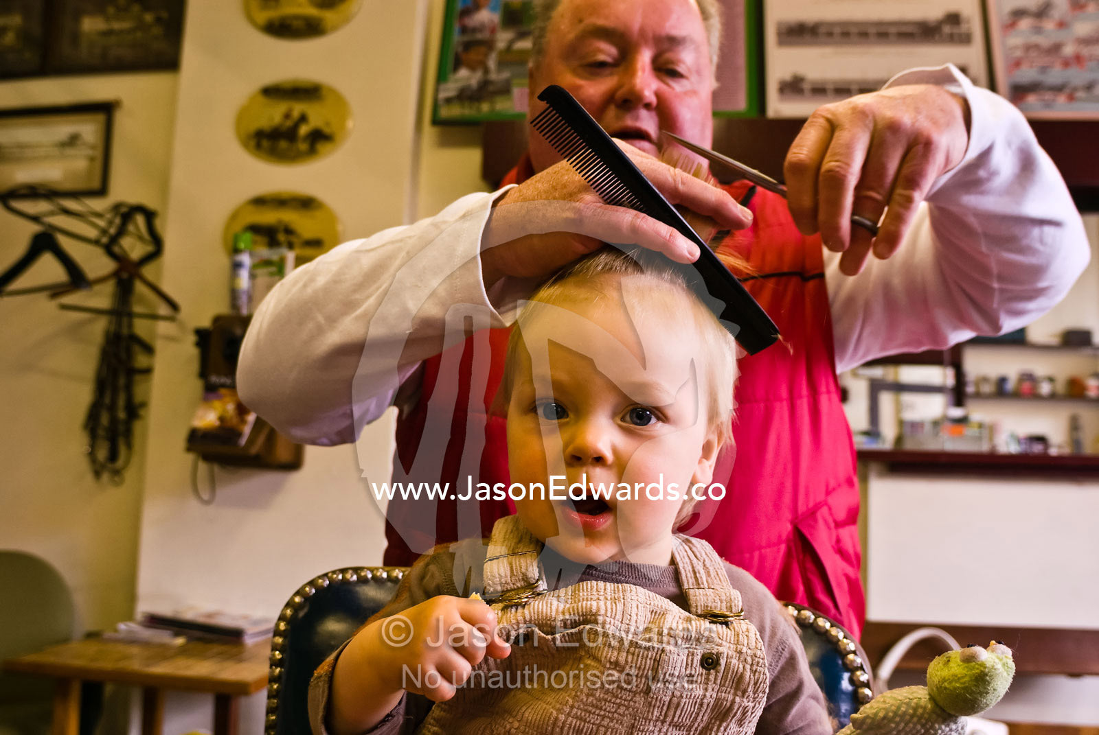 An amazed baby curiously watches a barber give him his first haircut. Melbourne, Victoria, Australia.