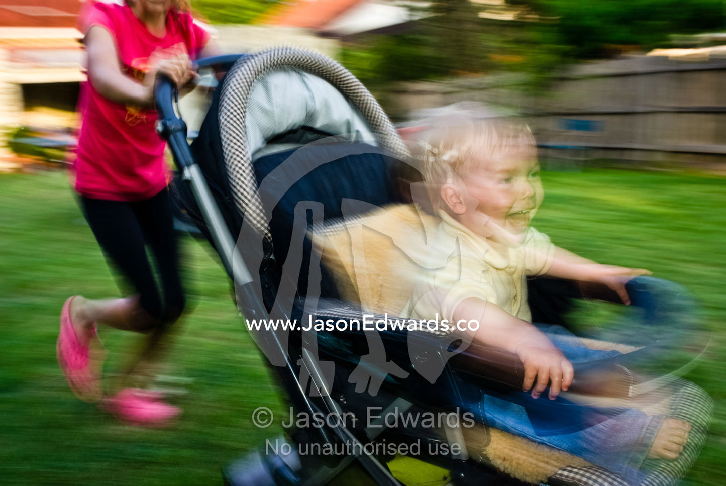 An ecstatic baby races around a yard in a stroller with his cousin. East Malvern, Victoria, Australia.