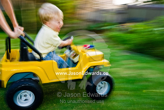 An ecstatic baby races around a yard in a toy car with his cousin. East Malvern, Victoria, Australia.