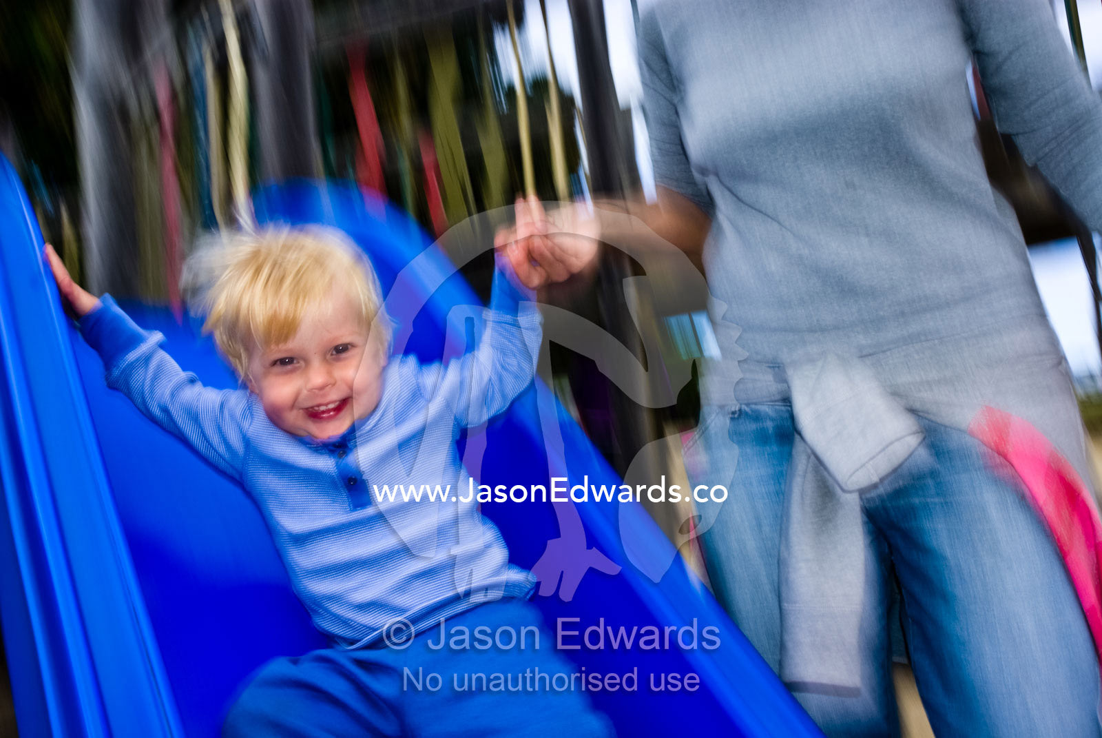 A young boy slips down a playground slide holding his mothers hand. Torquay, Victoria, Australia.