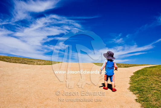 A baby climbs a steep hill towards a blue sky and new horizons. Torquay Point, Torquay, Surf Coast, Victoria, Australia.