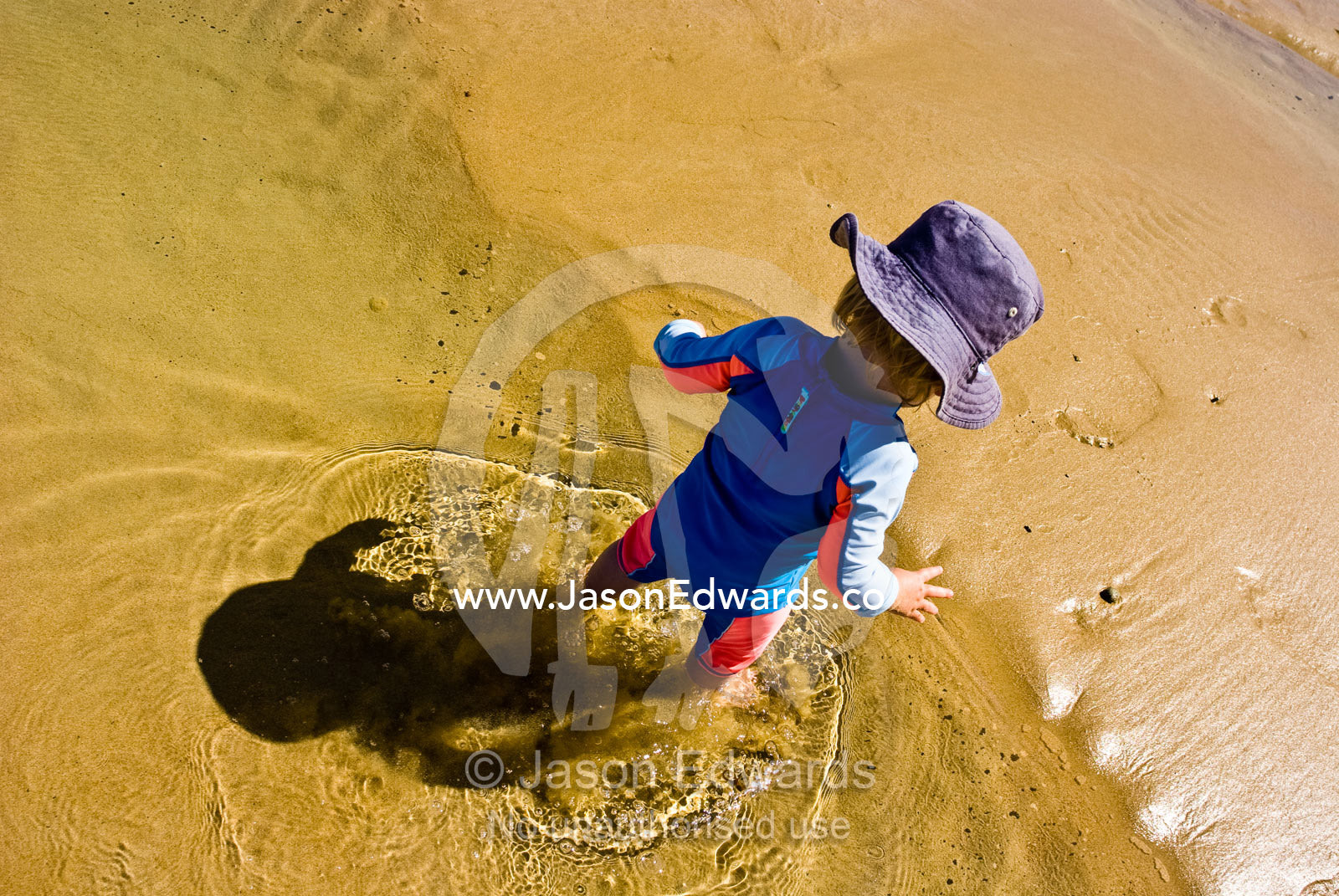 A  baby wades through the shallow water on a beach. Torquay Point, Torquay, Surf Coast, Victoria, Australia.