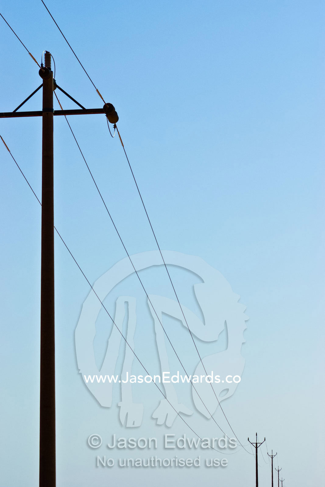 Telegraph poles and cables rise into the clear desert sky. north of Broken Hill, New South Wales, Australia.
