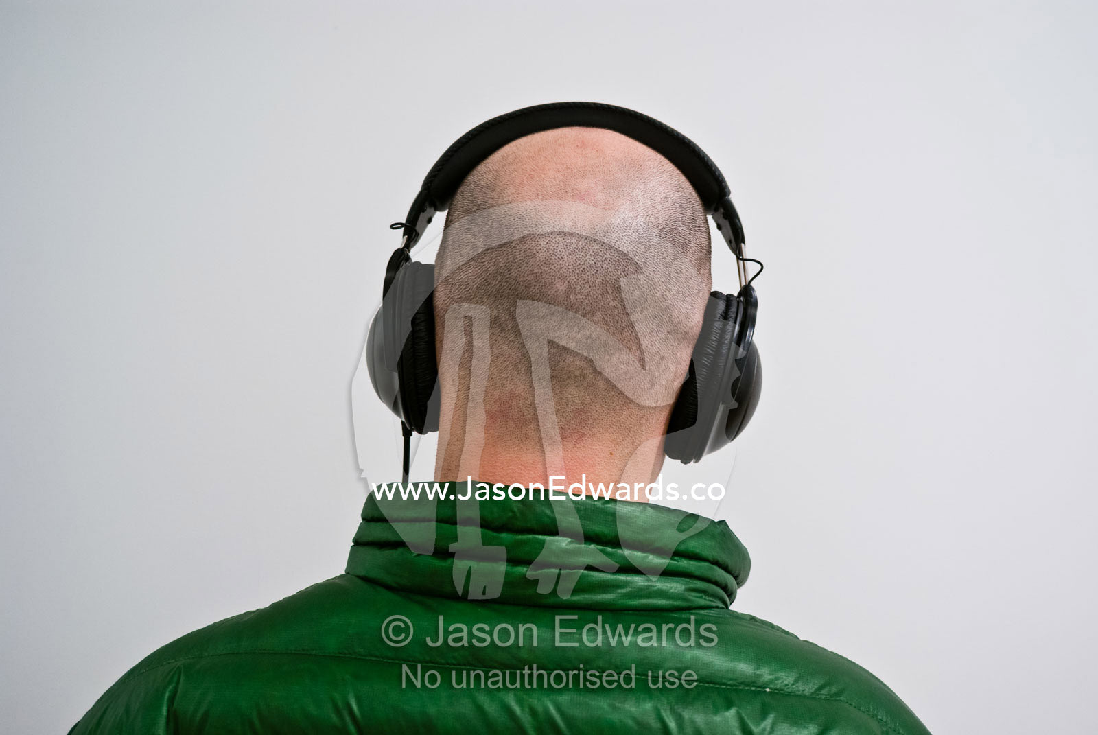 A funky guy in a green winter coat listens to music via headphones. Washington, District of Columbia.
