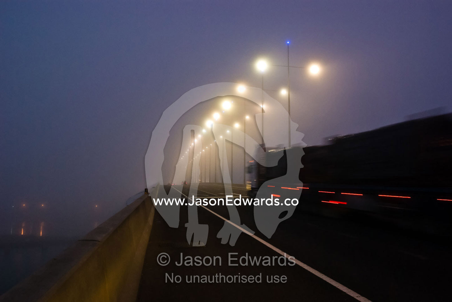 In pre-dawn light a large truck passes through heavy fog on a bridge. Bolte Bridge, Yarra River, Melbourne, Victoria, Australia.