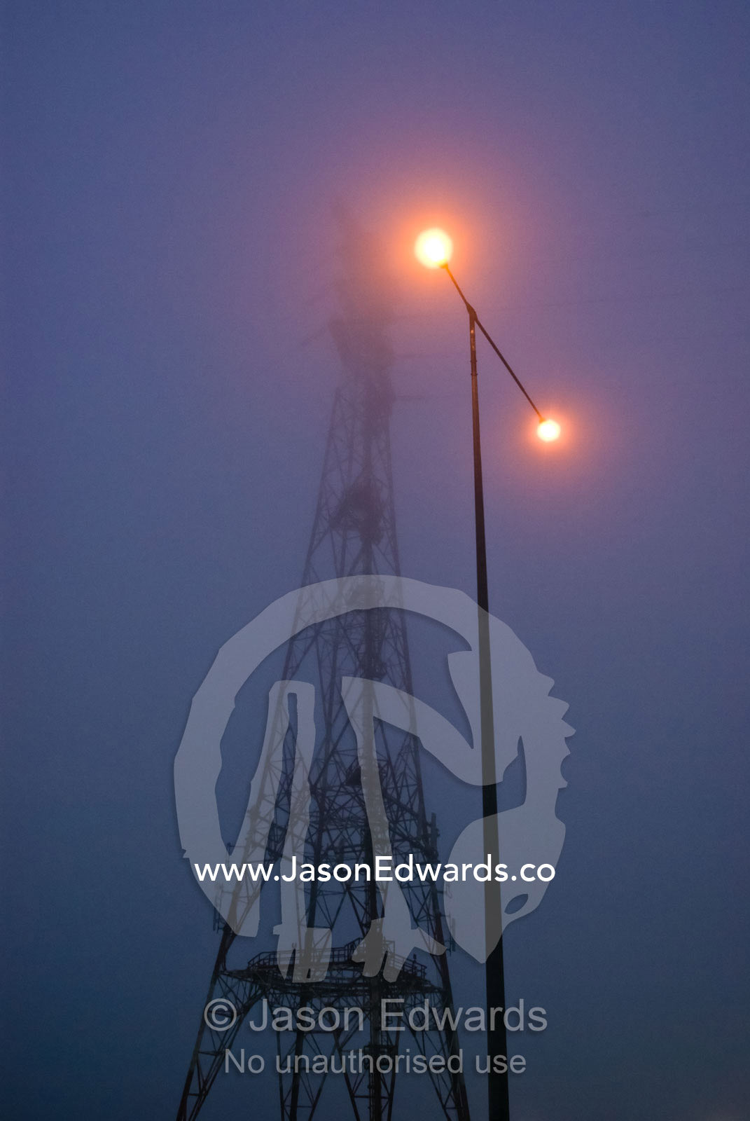 An electricity tower and freeway lighting emerge from heavy fog. Bolte Bridge, Yarra River, Melbourne, Victoria, Australia.