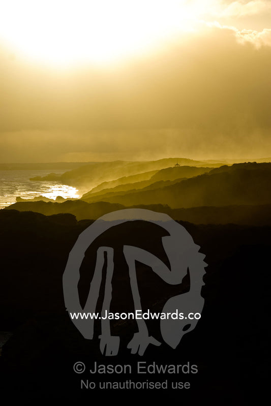 Storm clouds and golden sea mist engulf a rugged coastline at sunset. Mornington National Park, Victoria, Australia.