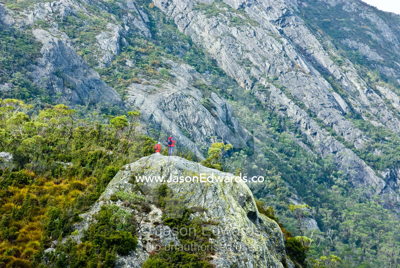 Hikers on a granite escarpment gaze at majestic glacial mountains. Dove Lake, Cradle mountain Lake St Clair National Park, Tasmania, Australia.