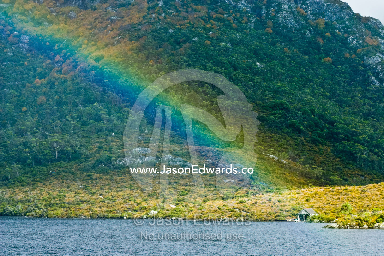 A rainbow descends onto an alpine lake touching an antique boathouse. Dove Lake, Cradle mountain Lake St Clair National Park, Tasmania, Australia.