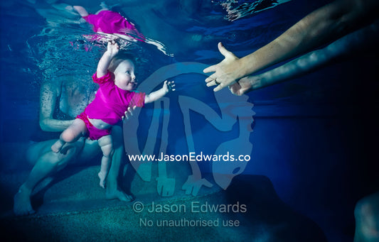 A baby reaches out for her mother's hands whilst learning to swim. Vaucluse Hospital, Brunswick, Victoria, Australia.