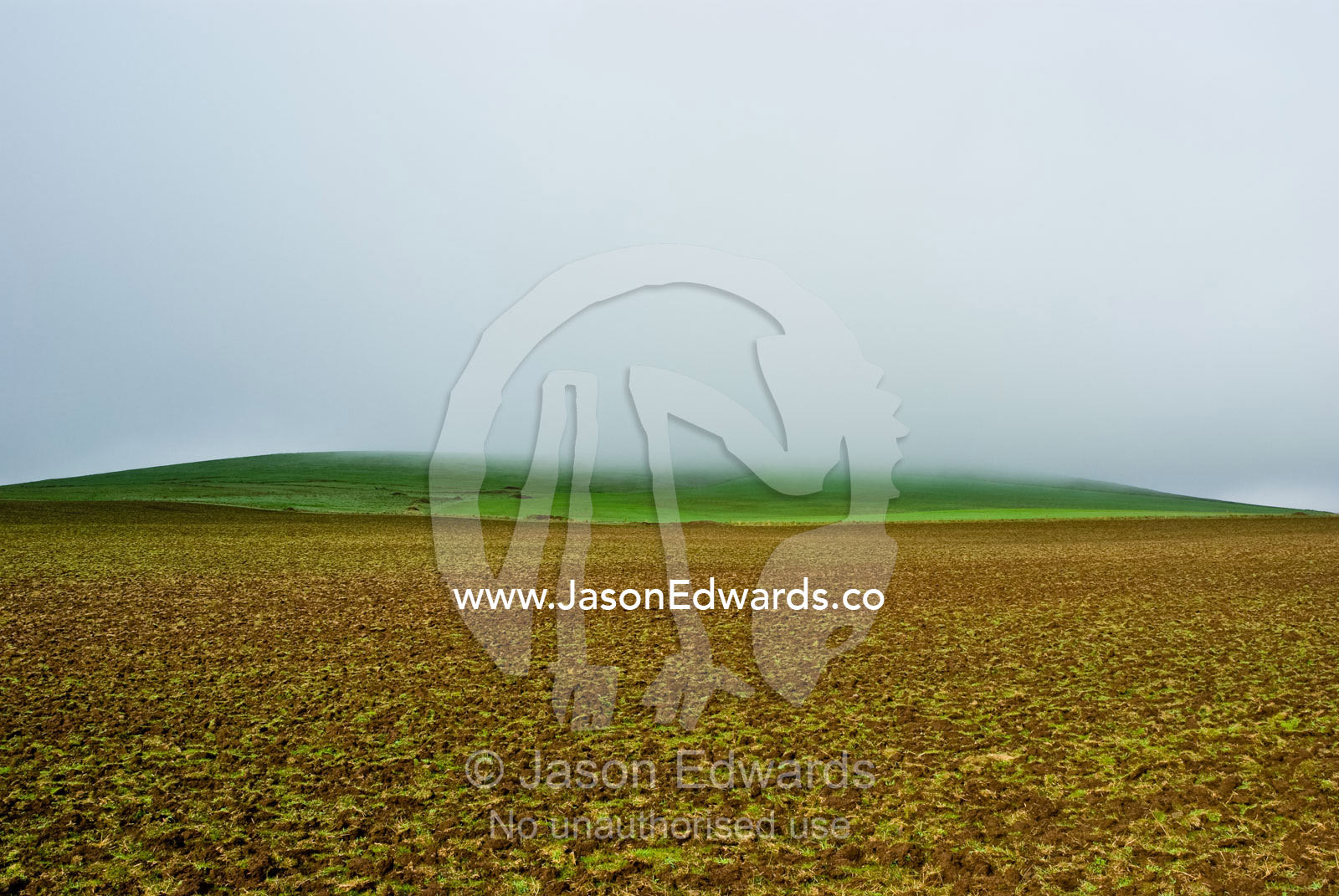 Mist and rain descend on a small hillock over newly ploughed farmland. near Basalt, Daylesford District, Victoria, Australia.