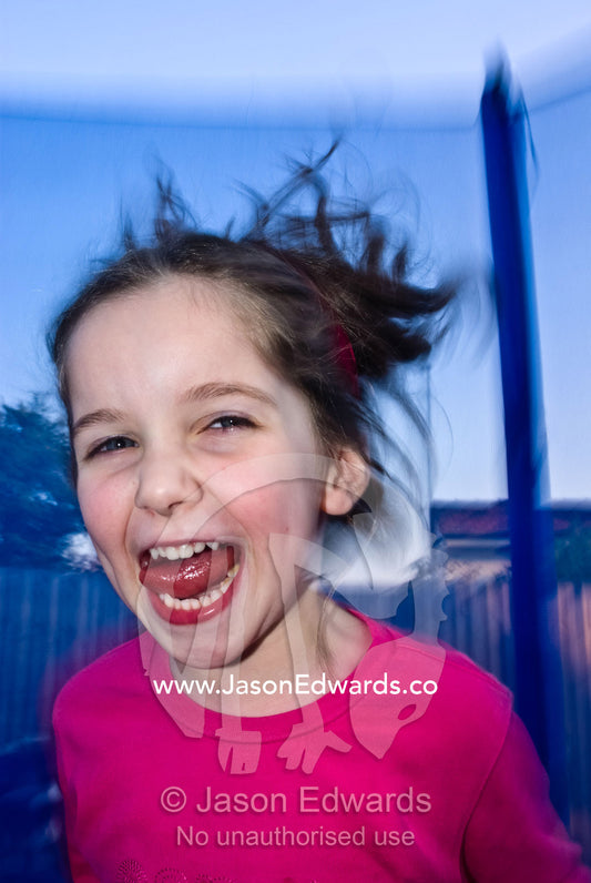 A young girl laughs as she bounces ecstatically on a trampoline. Mount Waverley, Victoria, Australia.