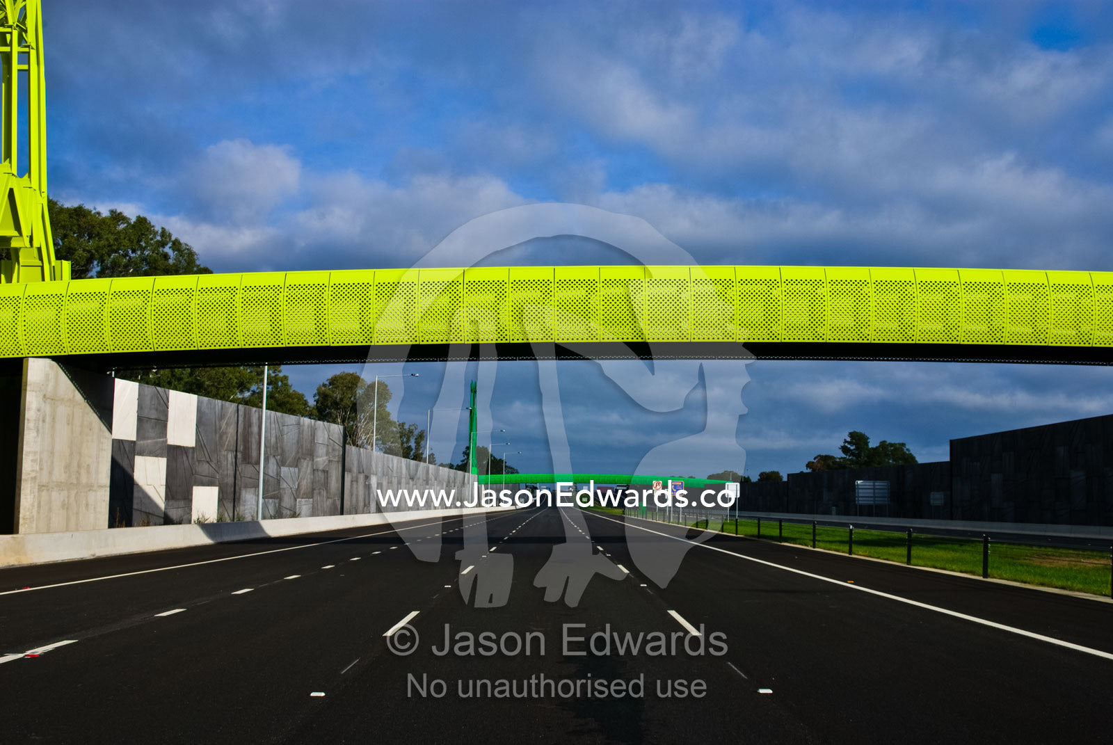 A funky lime green pedestrian footbridge spans an empty freeway. Eastern and Southeastern Suburbs, Melbourne, Victoria, Australia.