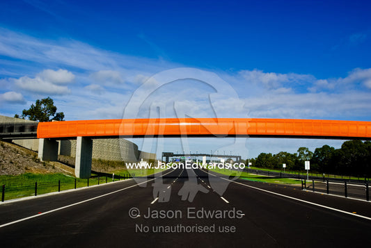 A funky bright orange pedestrian footbridge spans an empty freeway. Eastern and Southeastern Suburbs, Melbourne, Victoria, Australia.