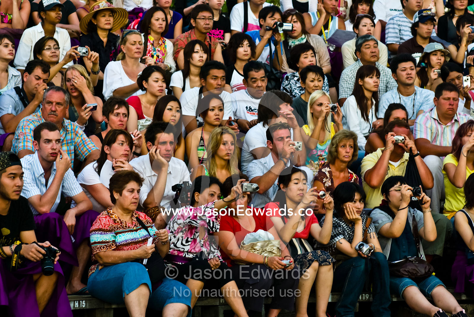 A crowd of enthralled tourists photograph a Kecak Monkey Dance. Pura Luhur Temple, Uluwatu, Badung Regency, Bali, Indonesia.