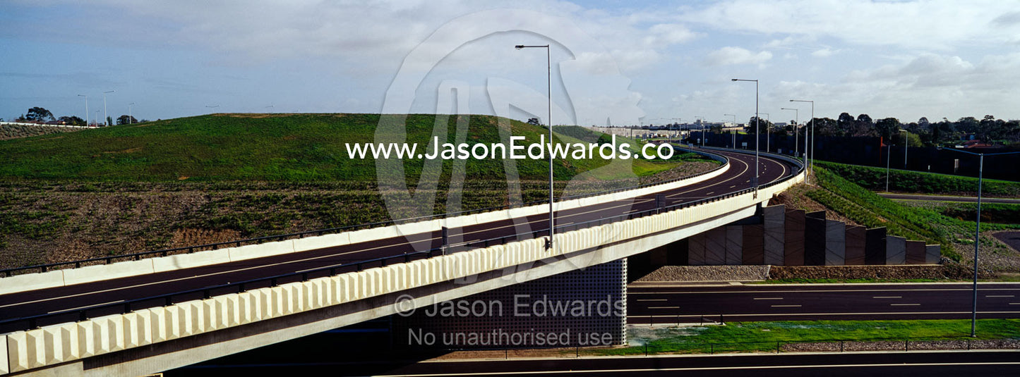 A deserted broad sweeping exit bridge dissects an empty freeway. Eastern and Southeastern Suburbs, Melbourne, Victoria, Australia.