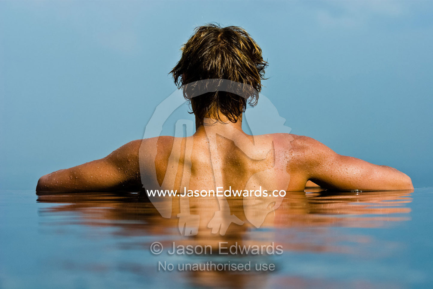 A young man enjoys the tropical sun in a horizon swimming pool. Bingin, Bali, Indonesia.