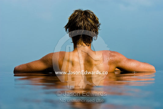 A young man enjoys the tropical sun in a horizon swimming pool. Bingin, Bali, Indonesia.