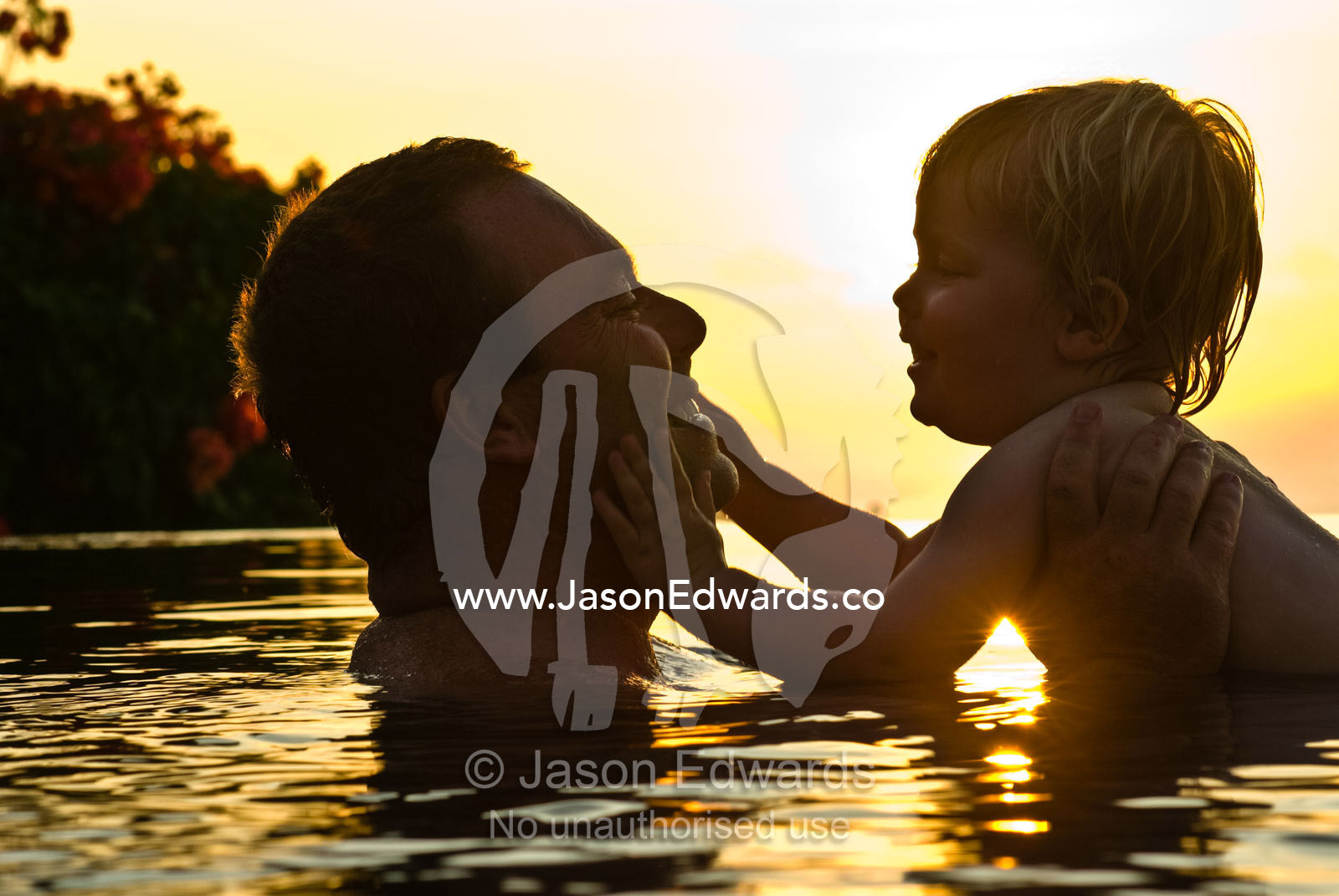 A father and son play lovingly in a tropical swimming pool at sunset. Bingin, Bali, Indonesia.