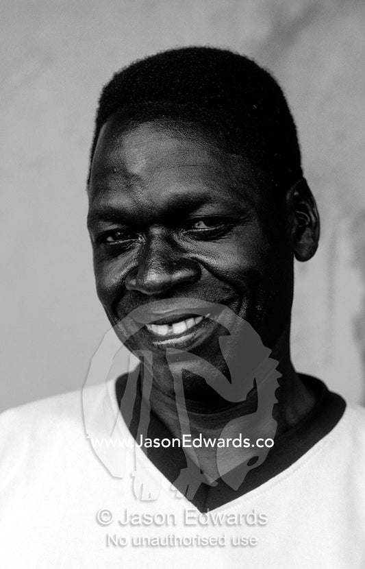 A smiling young East African man resting in a roadside truck stop. Tororo District, Eastern Uganda.