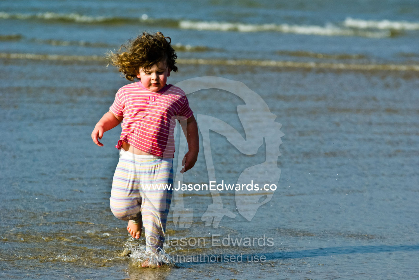 A toddler splashes through the shallows late on a summers afternoon. Cosy Corner, Torquay, Victoria, Australia.