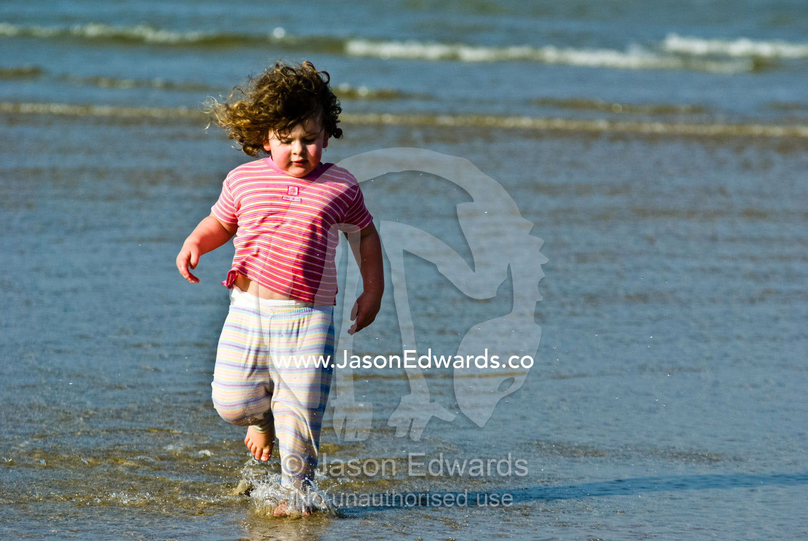 A toddler splashes through the shallows late on a summers afternoon. Cosy Corner, Torquay, Victoria, Australia.