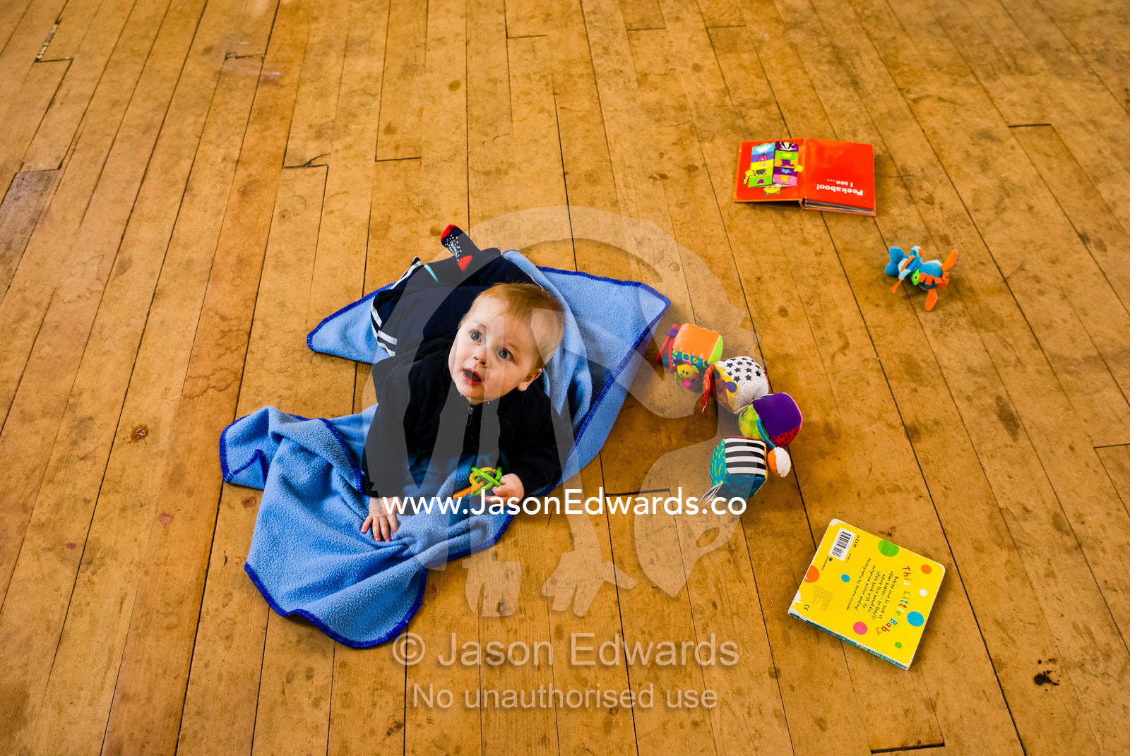 A baby shuffles around with his toys on the floor of a country hall. Glenlyon, Victoria, Australia.