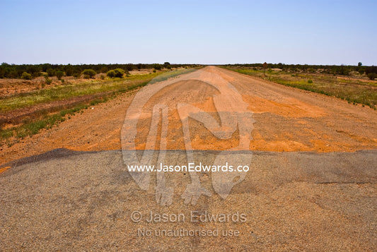 A bitumen road becomes a dirt track heading across the desert plain. Outback western New South Wales, Australia.