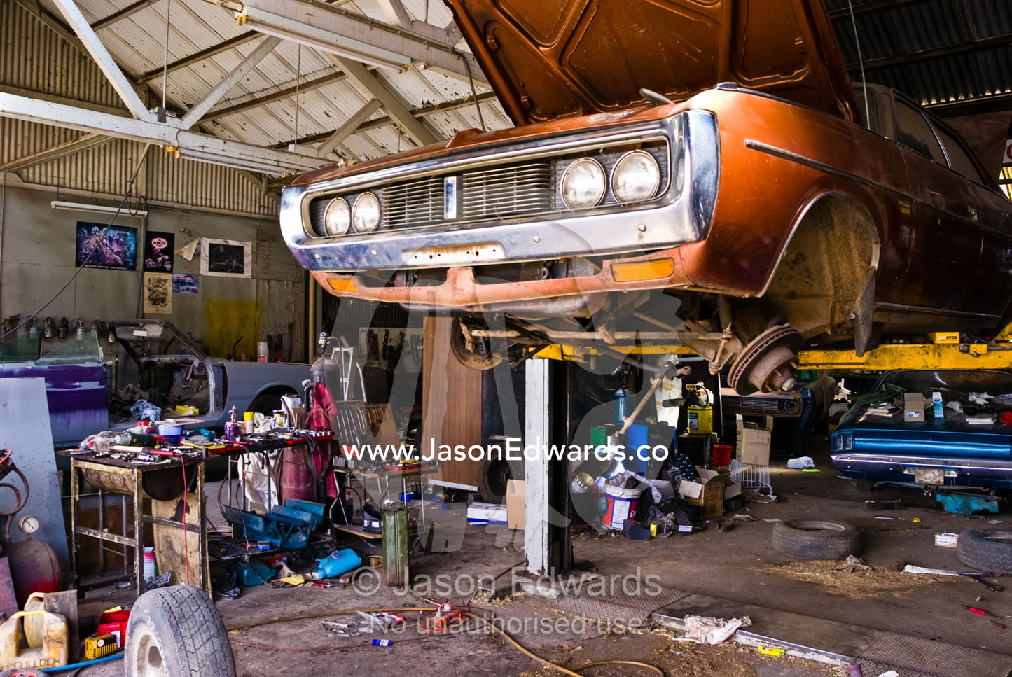 An old car rests on a hoist for repairs in a messy country workshop. Inglewood, Victoria, Australia.