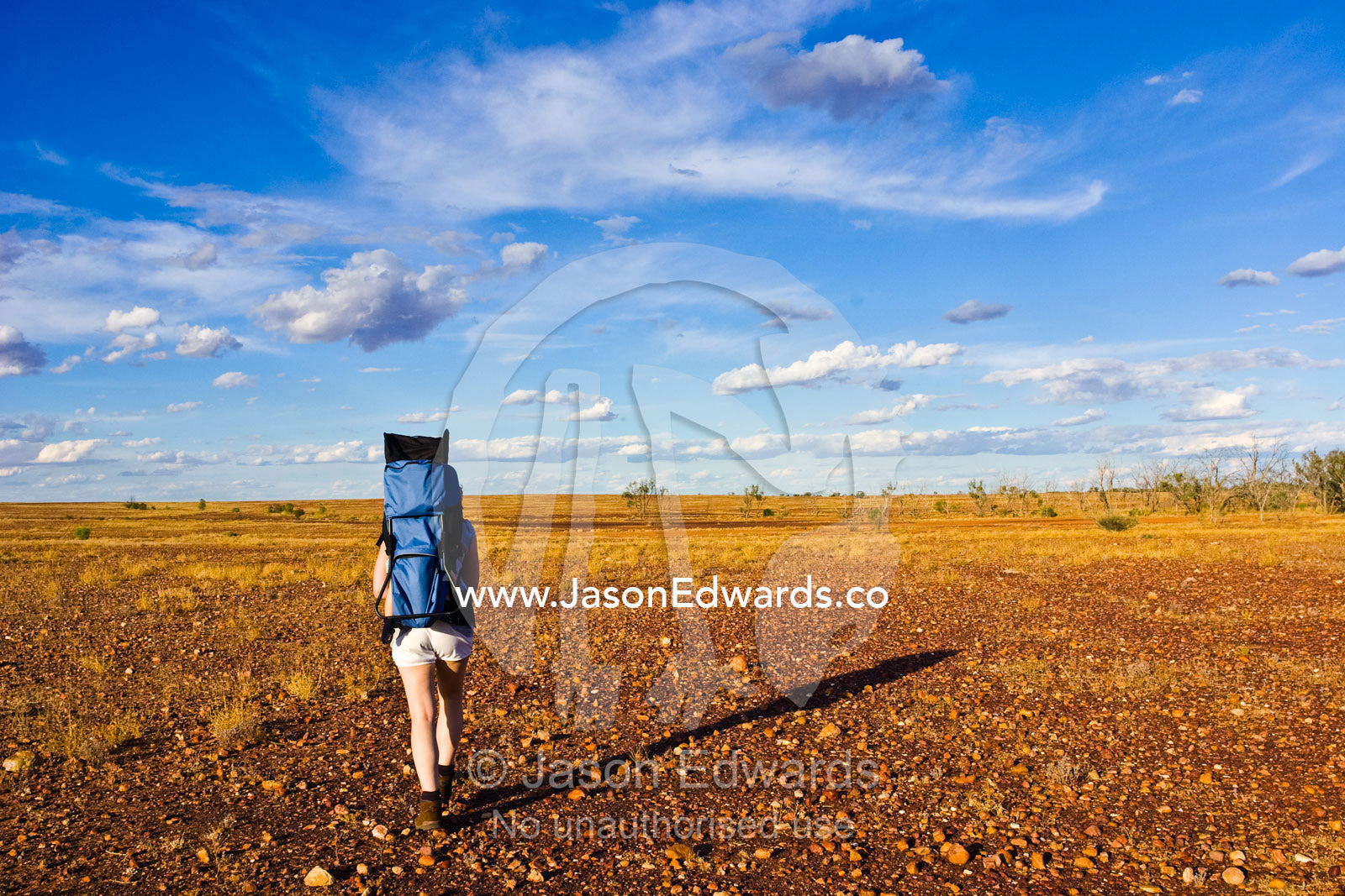 A mother carries her baby on her back whilst hiking in the outback. Sturt National Park, New South Wales, Australia.