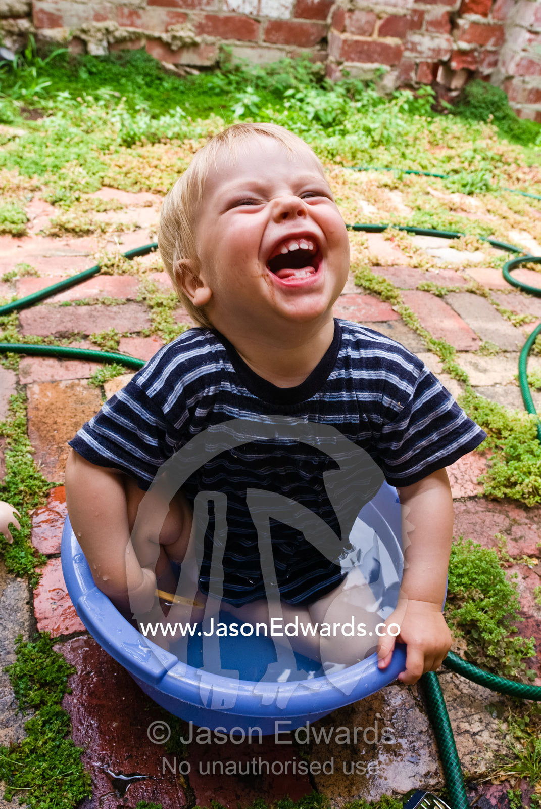 A toddler laughing hysterically whilst cooling off in a tub of water. North Carlton, Victoria, Australia.