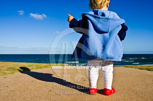 A toddler looks out to sea and the horizon from a hilltop on the coast Great Ocean Road,Torquay, Victoria, Australia.