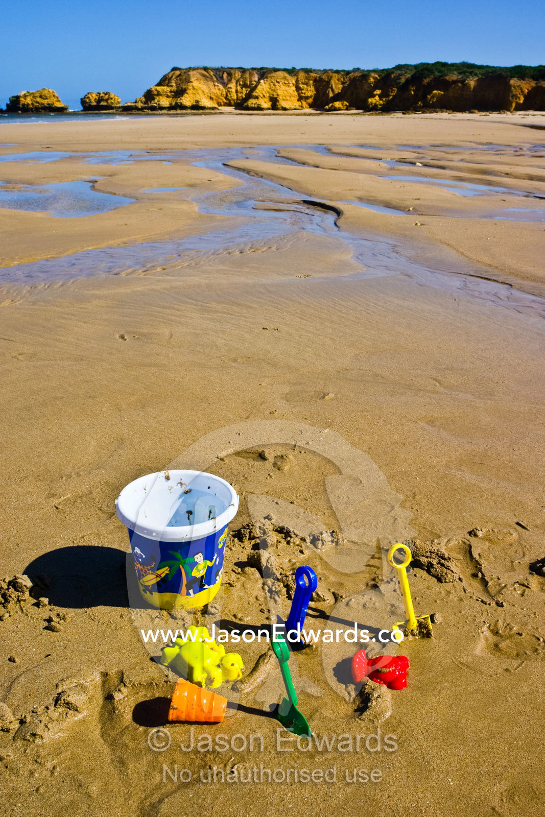 Child's beach toys, bucket and spade abandoned on the sand at low tide Haystacks, Torquay Point, Torquay, Victoria, Australia.