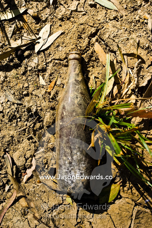 An old beer bottle lies in dry river mud exposed by the drought. Bullatail Creek, Mundiwa Station, Deniliquin, New South Wales, Australia.