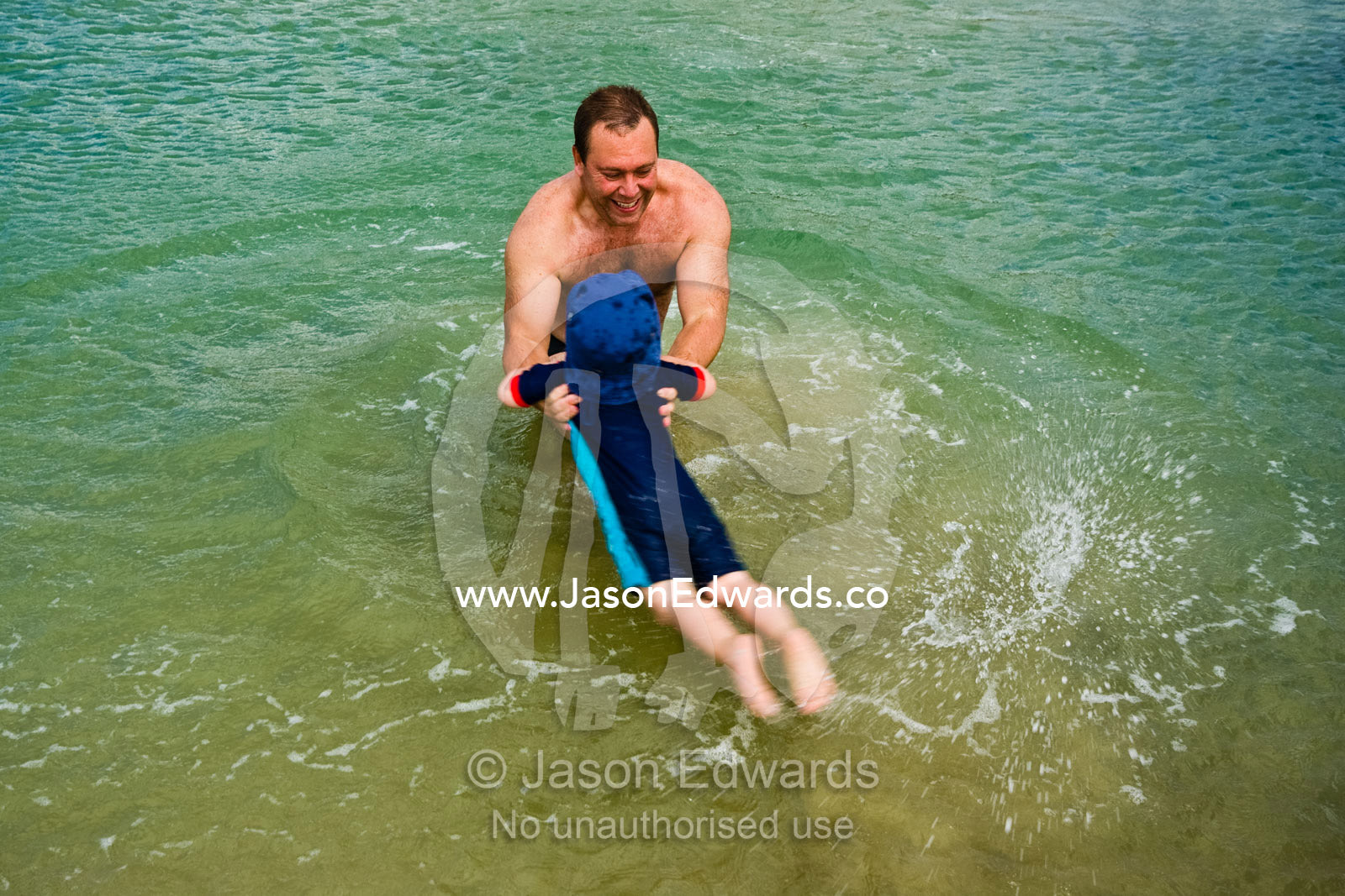 A father swings his small son through the shallows at the beach. Barwon Heads, Victoria, Australia